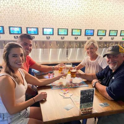 Inside, guests cheering with beers at a table in front of a beer tap wall